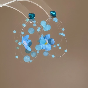 Detail of floral earrings featuring blue fabric petals and transparent beaded tassels