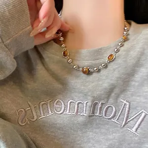 Gros plan du collier de perles en œil de tigre et perles argentées sur pull gris