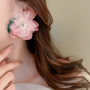 Detailed view of pink fabric flower earring with green leaves worn by a model