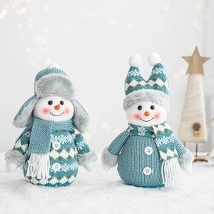 Detail of knitted snowman plush dolls with teal blue scarves and hats on white snow background