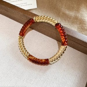 Detail of a geometric acrylic threaded bracelet with gold metal and amber tubes on a tray