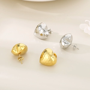 Macro detail of gold and silver heart stud earrings with hammered metal texture