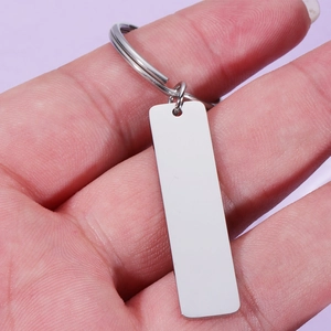 Polished stainless steel rectangular keychain tag held in hand on soft purple background
