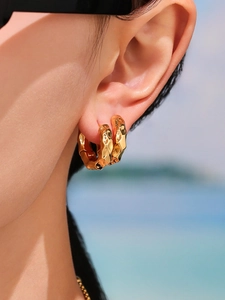 Détail de boucles d'oreilles créoles dorées irrégulières avec une texture de surface polie