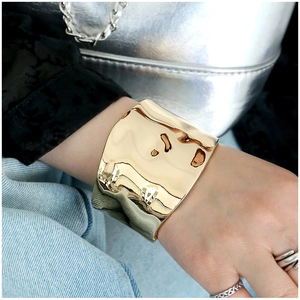 Polished gold irregular wide cuff bracelet with a glossy finish on a female wrist