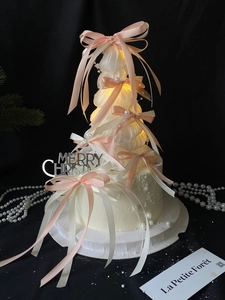 Detail of Christmas tree cake with pink silk bows and warm LED lights inside
