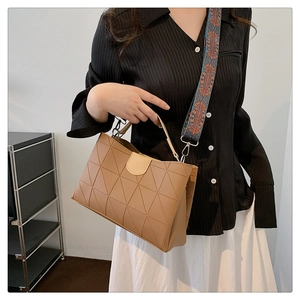 Detail of light brown geometric tote bag with patterned wide strap held by a model