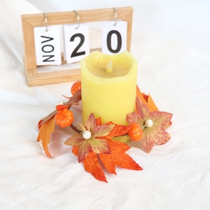 Detail of autumn candle ring featuring maple leaves and pumpkins around a yellow pillar candle