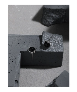 Detail of minimalist S925 silver stud earrings with black onyx stones on stone surface
