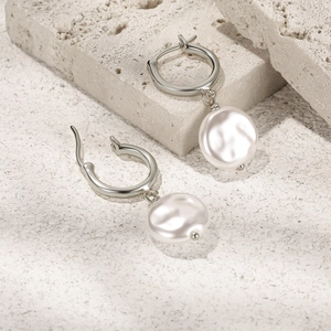 Detailed view of silver hoop earrings featuring elegant white pearls on a textured stone base