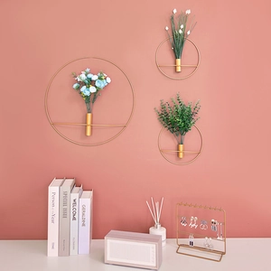 Set of three gold geometric circular metal wall vases with faux flowers on pink wall