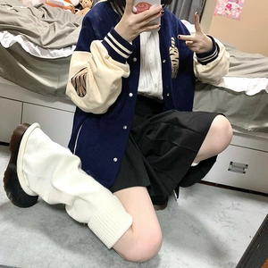 Close-up of white knitted leg warmers styled with a navy varsity jacket and a pleated skirt
