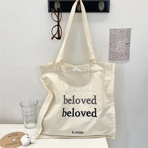 Detail shot of beloved embroidery on cream canvas tote bag with stylish accessories