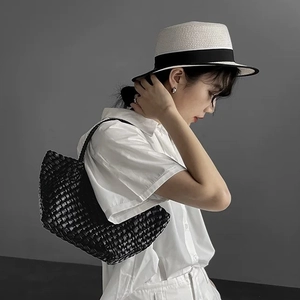 Detail of hand-woven black dumpling bag with wide-strip texture and top handle