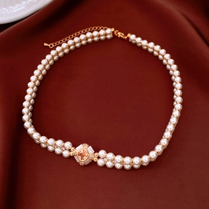 Detail of vintage double-layer pearl necklace with pink gemstone pendant on red silk