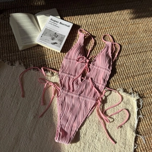 Dettaglio ravvicinato del costume intero rosa con trama a coste e lacci regolabili sul davanti