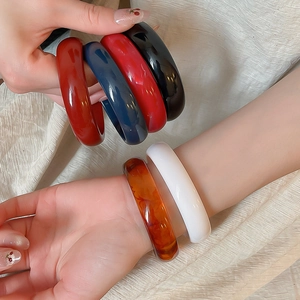 Detail shot of assorted colorful chunky resin bangles held by a hand on beige fabric