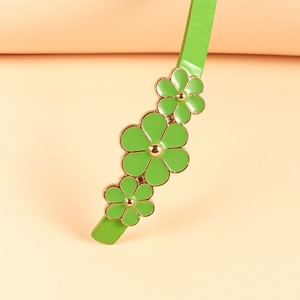Close-up of green leather belt featuring delicate enamel flower charms with gold edges