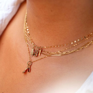 Close-up of layered gold necklace with square link chain and red gemstone pendant on model