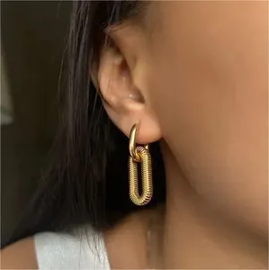 Detail of model wearing gold square chain earrings with elegant textured oval pendants