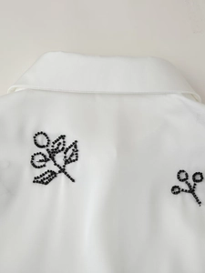 Close-up of elegant black beaded embroidery detail on a white satin lapel shirt fabric
