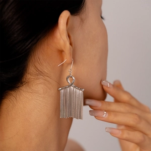 Close-up of elegant silver tassel drop earrings with a metallic knot design on model