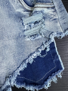 Dettaglio di pantaloncini di jeans a vita alta con bordi sfrangiati e patchwork su tela blu