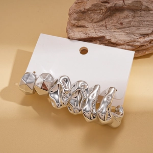 Detailed view of silver liquid metal earrings and geometric studs on warm background