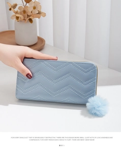 Detail of light blue long wallet featuring V-shaped quilting and a fluffy pom-pom charm