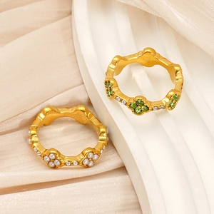 Detail of 18K gold clover rings with green crystals and pearls on silk background