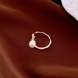 Detail view of gold bamboo-textured open ring with a teardrop pearl on brown satin