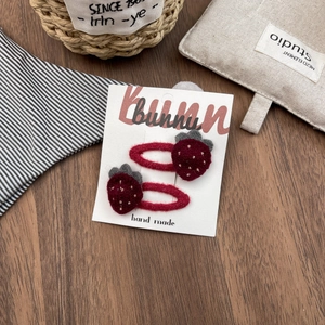 Detailed view of handmade felt strawberry hair clips with gold glitter on wood background
