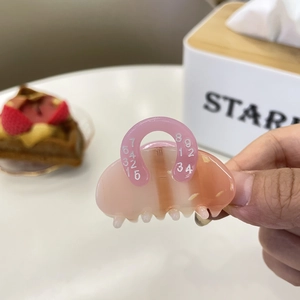 Mini pink acetate claw clip with numeric print held by hand in a cozy cafe setting