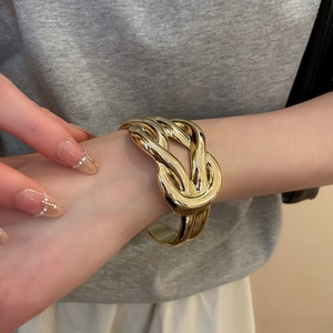 Close-up of a gold chunky knot cuff bracelet showing metallic texture and irregular fold design