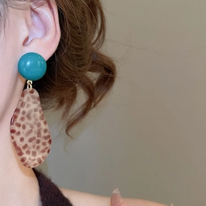 Close-up of leopard print teardrop pendant earring worn by a model in soft lighting
