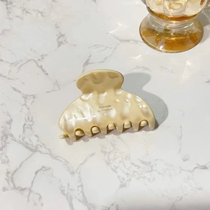 Close-up of cream acetate hair claw with Barrette la France text on marble surface