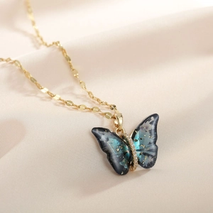 Macro shot of gradient blue butterfly pendant necklace with golden chain on satin