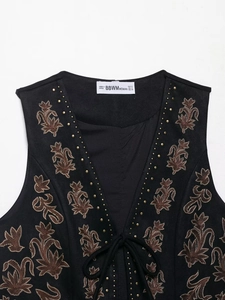 Close-up of black suede vest with brown vintage embroidery and golden rivet details