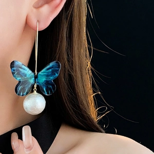 Elegant blue butterfly earrings with white pearl pendants worn by a model in a close-up