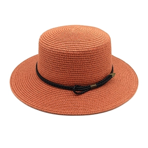 Close-up of rust red flat-top boater hat with black woven rope and bronze buckle detail