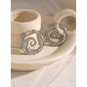 Vue macro de boucles d'oreilles spirales argentées sur un support minimaliste