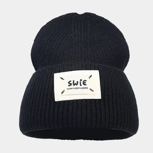 Close-up of black ribbed knit beanie with white embroidered letter patch and thick texture