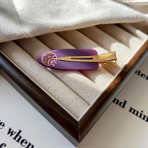 Détail d'une pince à cheveux en acétate violette avec motifs lune, étoiles et strass