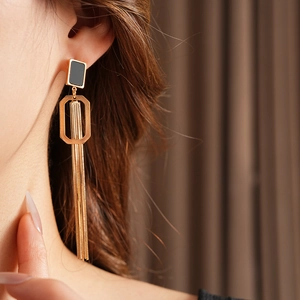 Gros plan de boucles d'oreilles pendantes dorées avec détail carré noir sur un mannequin