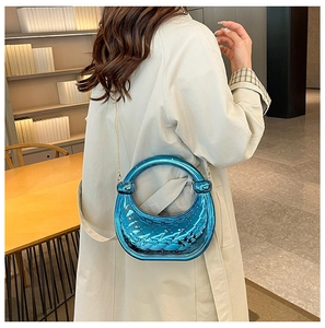 Detail of a shiny blue crescent handbag with quilted pattern held by a model in a trench coat