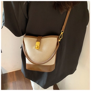 Detail showing brown and beige canvas bucket bag with gold hardware on a model