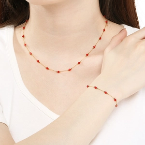 Detailed view of model wearing a delicate gold clover necklace and bracelet set with red beads