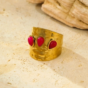 Close-up of wide gold textured ring with three red teardrop stones on stone background