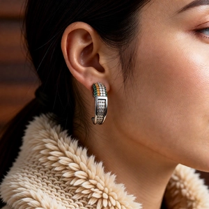 Detailed shot of C-shaped silver earrings with green and orange zircon stones on model