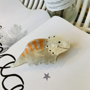 Detail of cute acrylic dinosaur hair claw clip in beige and orange with smooth texture